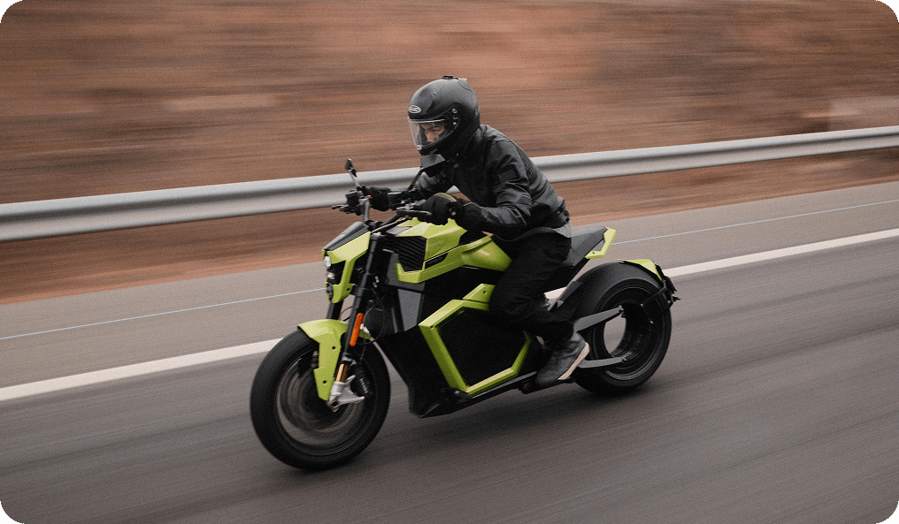 Rectangle 338 Person in black riding a bright green motorcycle at speed on a highway. The rider wears a helmet and leather jacket. The background is a blur, emphasizing motion, with a guardrail visible. The road appears slightly wet.