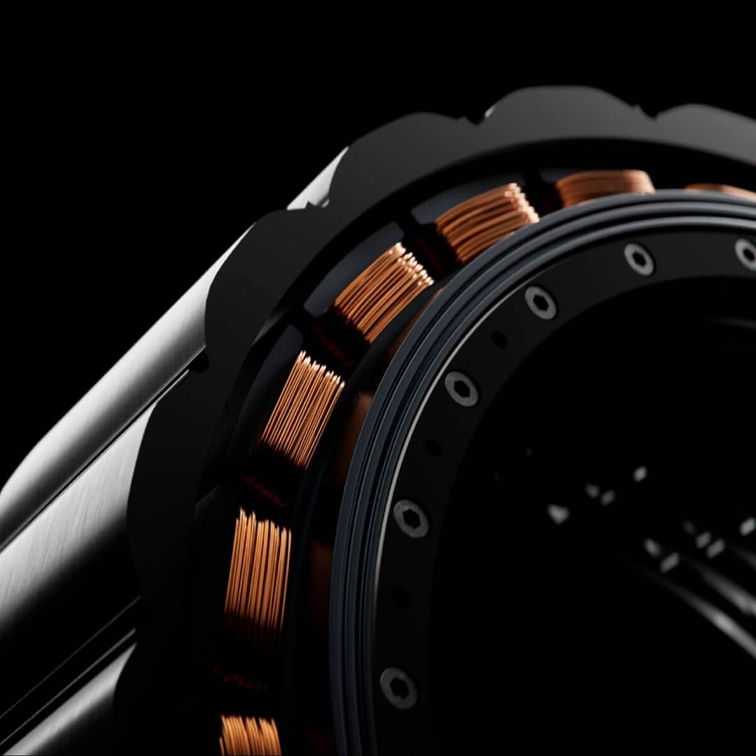 Close-up of a mechanical component featuring copper coils wound around a central structure. The metallic surface has a smooth, polished finish with a series of bolts and a black background, highlighting the intricate engineering detail.