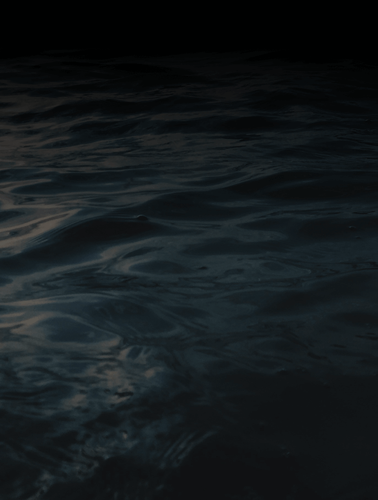 Dark, rippling water with subtle reflections under low light, creating a serene yet mysterious atmosphere.