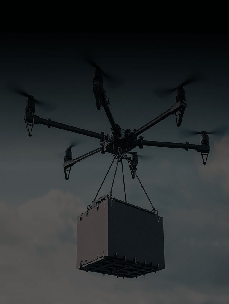 A drone with six rotors is carrying a large, rectangular package suspended below it against a cloudy sky.