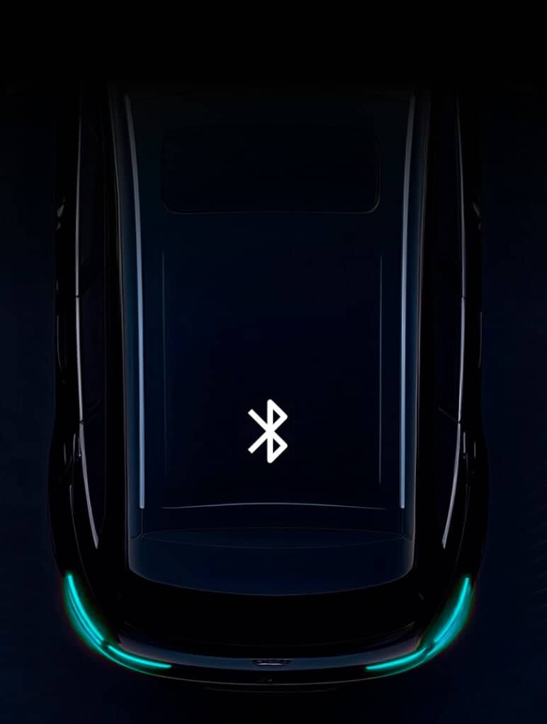 A top-view of a dark-colored car with a glowing Bluetooth symbol on the roof, surrounded by a dark background. The car's rear lights are slightly illuminated in a teal hue.