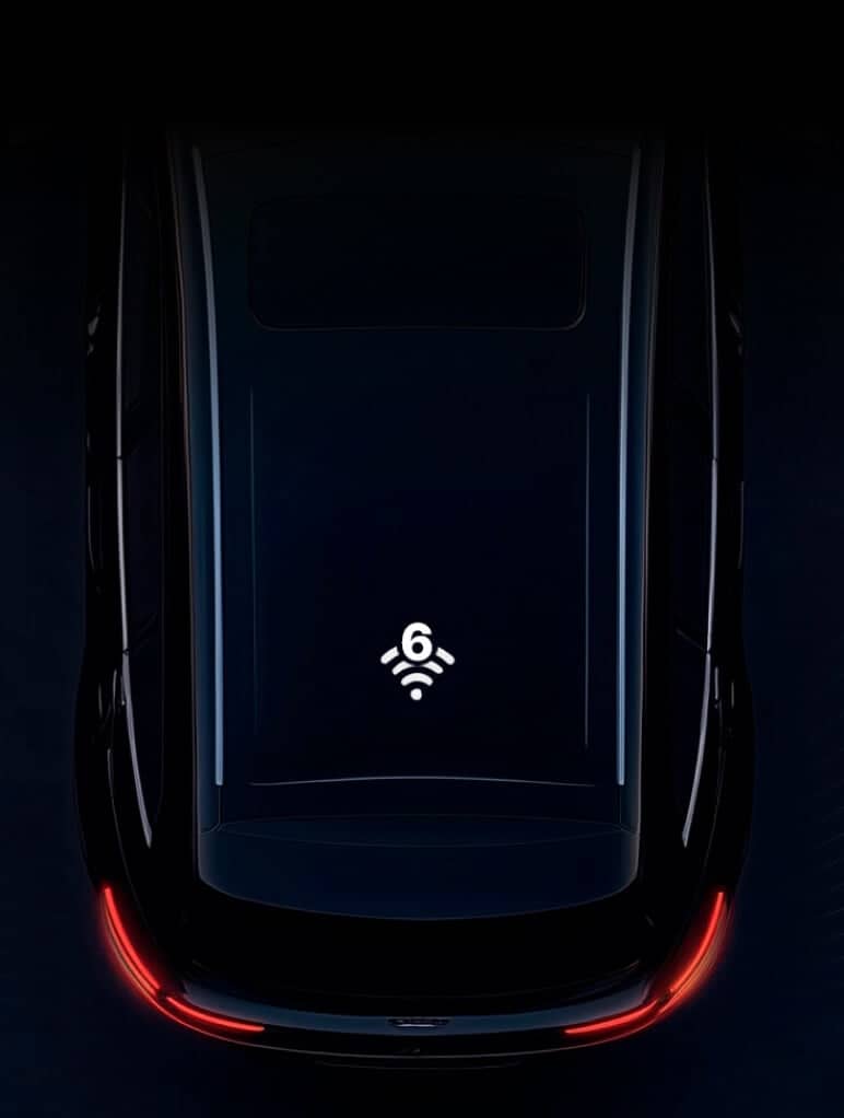A darkly lit image of a car roof, showcasing a Wi-Fi 6 symbol in the center, suggesting connectivity. The car's rear lights create a red glow at the bottom, adding contrast to the sleek, reflective surface.